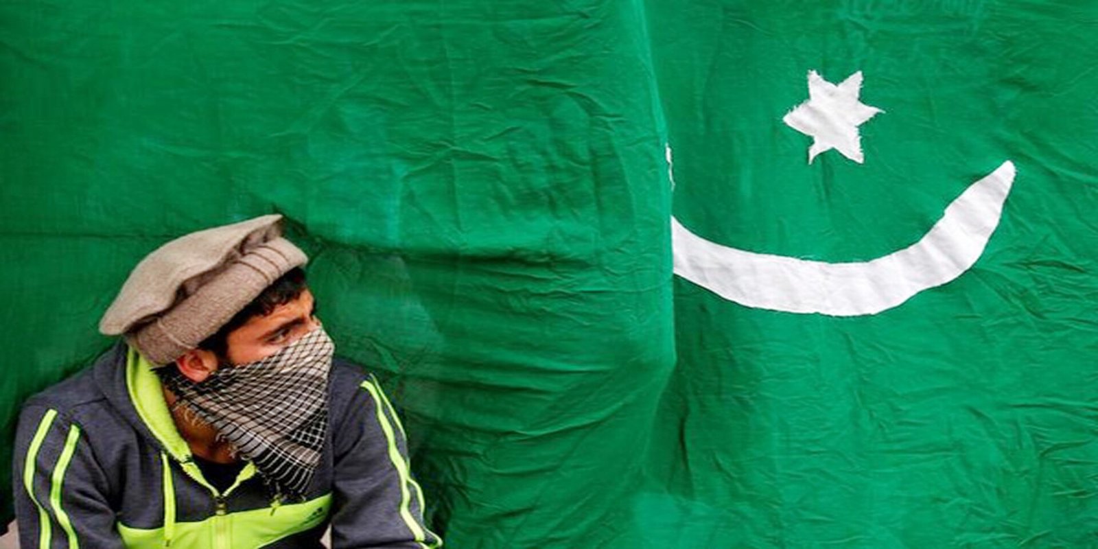 A masked protester sits next to a flag of Pakistan during an anti-Indian protest in Srinagar